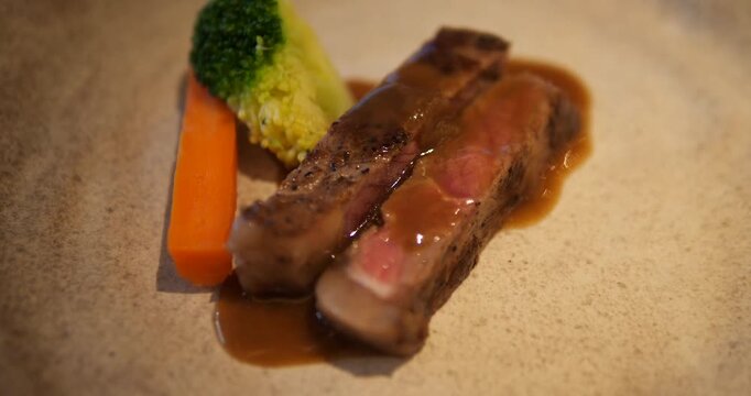 Cinematic close-up of premium medium-rare beef steak sliced and topped with savory gravy sauce, served with broccoli and carrot on a ceramic plate