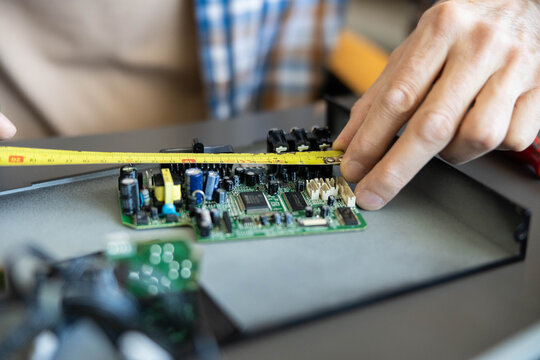 Technician's hands measuring a green circuit board with a tape measure, working on electronics component during maintenance