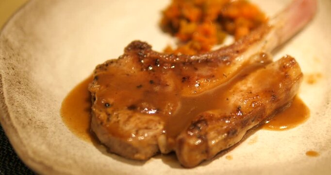 Cinematic close-up of premium grilled bone-in pork chop steak topped with rich gravy sauce, luxury restaurant fine dining gastronomy concept