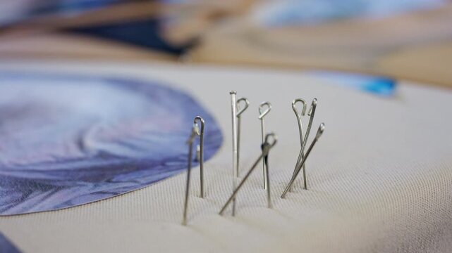 Close up of a hand placing several metal sewing pins into beige fabric beside a blue paper or fabric pattern