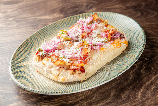 Delicious pinsa romana with red onions, bacon, melted cheese, and grated parmesan served on a green ceramic plate.