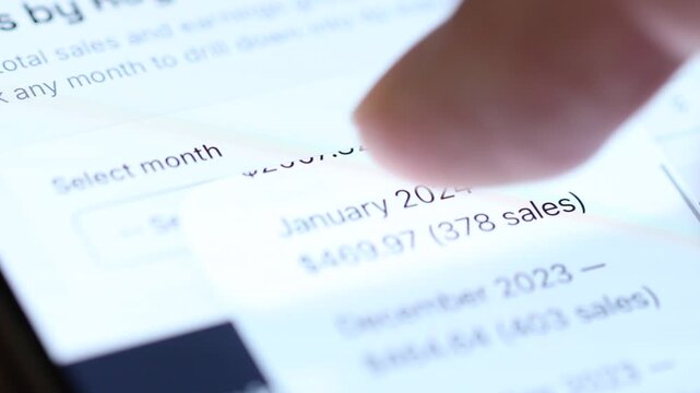Close-up 4K view of a finger tapping a "Select Month" drop-down menu on a phone screen, revealing sales revenue and performance history.