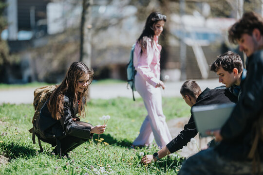 A group of school friends gather outdoors on grass, picking dandelions and interacting. Students relax and study together in a casual spring setting.