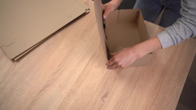 Female Hands assembling a brown cardboard box, top view. process of sustainable business and eco-friendly logistics.