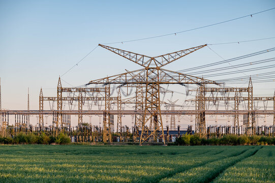 Electrical substation with extensive high-voltage power grid infrastructure in rural landscape. Electrical substation with steel lattice structures, transmission lines and switching equipment.