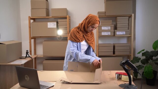 Muslim woman assembling Cardboard box for shipping orders. Working in small home office.