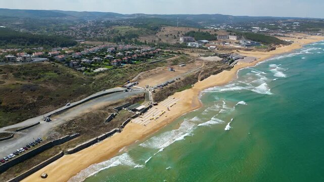 Aerial view flying along a scenic coastal road running parallel to a golden sand beach and rolling turquoise ocean waves showcasing the ultimate summer road trip travel destination