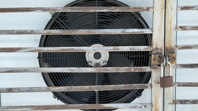 White air conditioner behind rusted grate showing industrial condenser unit enclosed behind weathered metal grille with visible