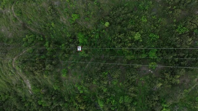 Aerial view of the modern cable car system in Tbilisi, Georgia, showing the upper station building, ropeway cables, and lush green hills under a dark cloudy sky