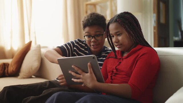 Happy Black teen boy and his sister watching short videos on tablet, leisure