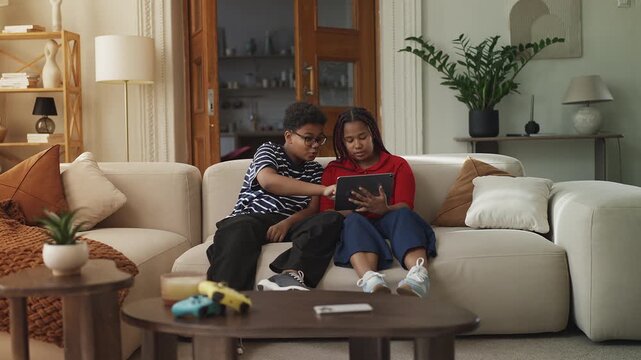 Joyful African American girl and boy playing educational game on tablet at home