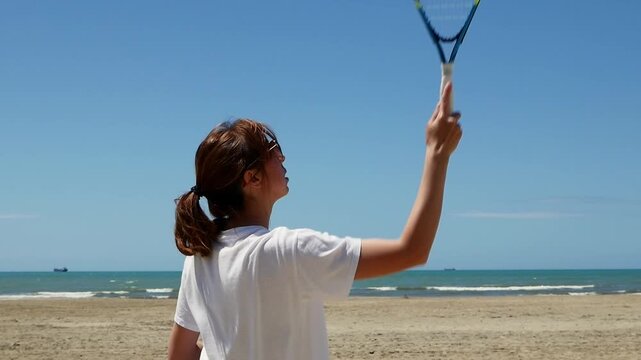 Woman returning shuttlecock in speed badminton on sandy beach , summer fun, outdoor game, active lifestyle.