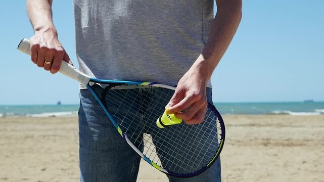 Man practicing speed badminton serve on beach, summer outdoor training, shuttlecock action, fitness, active lifestyle, dynamic sports.