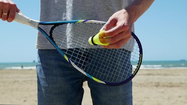 Man practicing speed badminton serve on beach, summer outdoor sport, athletic training, shuttlecock in motion, active lifestyle, fitness, dynamic sports action.