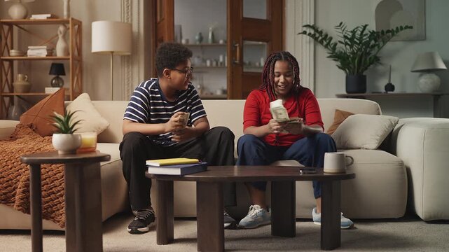 African American siblings counting money at home and high-fiving each other