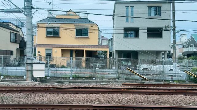 Typical Japanese residential houses line the railway track in Shinagawa district of Tokyo. Small multistory buildings stand extremely close to each other along a narrow suburban street.