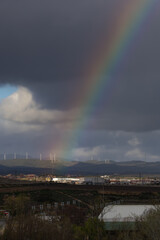 Fototapeta premium Distant view of wind turbines on a hill under a dramatic sky with a bright rainbow, concept of green renewable energy and sustainable environment