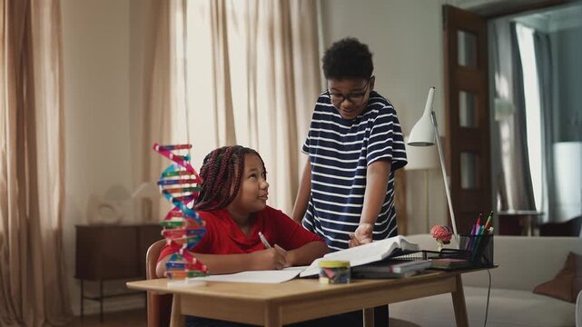 African American boy teasing his diligent sister while she does homework