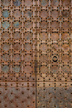 Full frame texture of a weathered and rusted metal door featuring a repetitive geometric quatrefoil pattern and studs