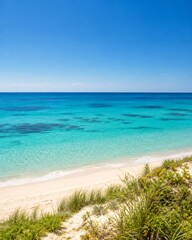 Obraz premium Idyllic tropical beach scene featuring translucent turquoise ocean water meeting a soft white sandy shore with green dune grasses