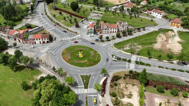 Aerial view of a suburban roundabout with landscaped green center and cars driving surrounded by rural houses with terracotta roofs and green farmland in the Portuguese countryside