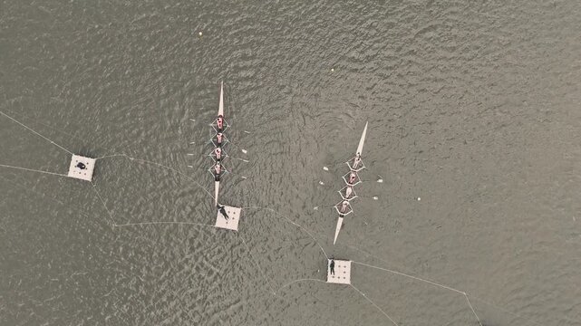 Overhead aerial view of rowing sculls with teams of rowers at the starting docks on a calm river preparing to race with floating platforms and mooring lines visible from above