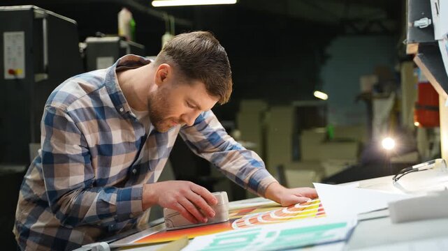Printing house worker checking color quality of poster