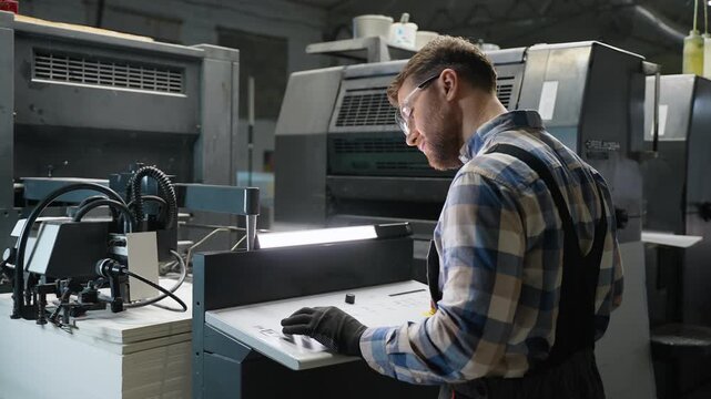 Printing house worker operating industrial printing machine