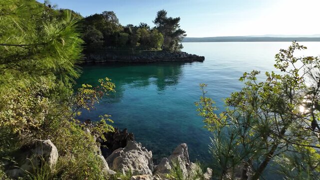 Rocky Adriatic Sea coastline with Mediterranean pine trees and turquoise water near Malinska - Krk Island, Croatia. Panning view from the Paradise Coastal Trail or seaside promenade on a sunny day.
