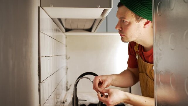 Young man in overalls diligently working on a kitchen renovation, meticulously applying grout with a small tool to the seams between white ceramic tiles for a fresh backsplash