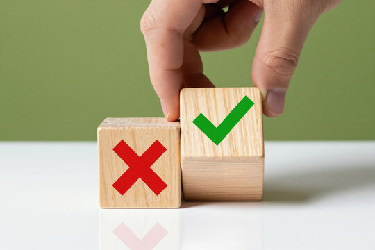 Hand turns wooden cube from red cross mark to green checkmark. Symbolizes making decision choice between approval and rejection. Business concept for yes or no.