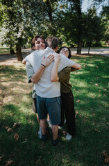 Fototapeta premium Three friends embrace in a park, sharing a warm group hug and smiling. A joyful outdoor moment with close friends hugging on grass under trees.