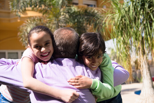 Modern family father hugging smiling children outdoors in warm backyard moment of affection and joy