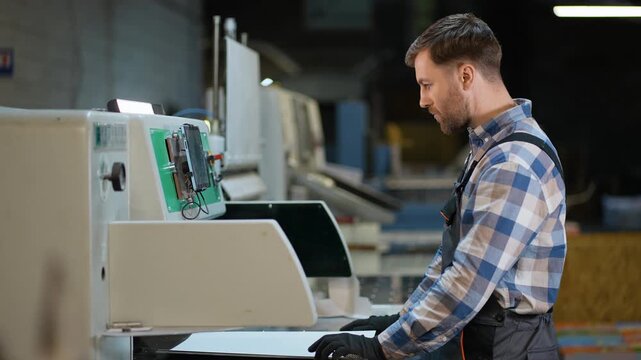 Factory worker operating industrial printing machine at print plant