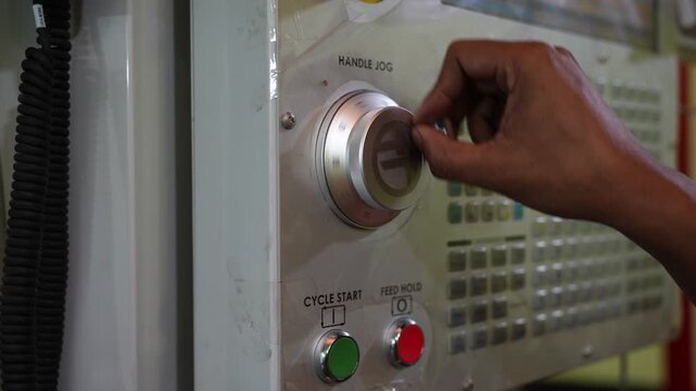 Bogura, Bangladesh - 04 January 2024: View of a worker's hand turning a jog dial on an industrial CNC machine control panel in a manufacturing facility.