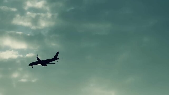Commercial passenger airplane landing with gear down in cloudy overcast sky. Silhouette of twin-engine jet airliner flight in foggy weather, aviation transport and tourism travel background.