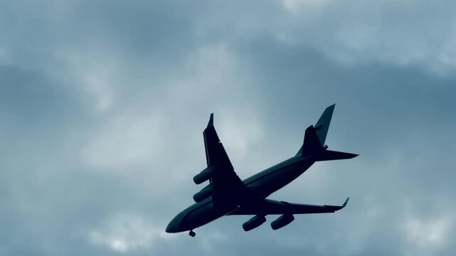 Large four-engine airplane flying high in cloudy overcast sky close up. Silhouette of commercial passenger jet or cargo aircraft takeoff in foggy weather, aviation and air travel background.