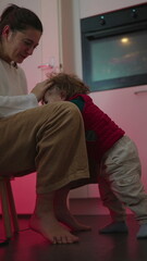Obraz premium Playful mother holding young child upside down across her lap while smiling during joyful bonding moment at home