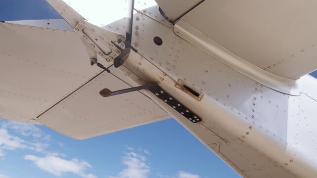Detailed underside view of aircraft tail, wing structure and mechanical flap linkage against blue sky, highlighting aviation engineering and airplane component design. Anti tail strike