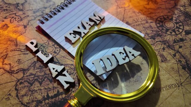 A magnifying glass focuses on the word 'IDEA' through a spiral notebook on a map.