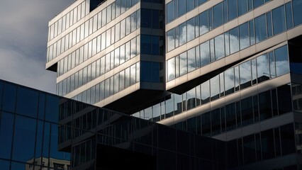 Obraz premium Modern glass office building with reflective windows under cloudy sky