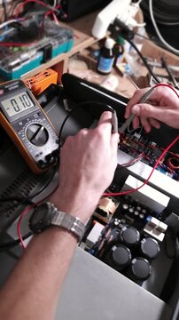 A technician uses a digital multimeter to probe an open electronic device on a cluttered workbench, checking circuit board components. Concept of electronics repair and technical maintenance