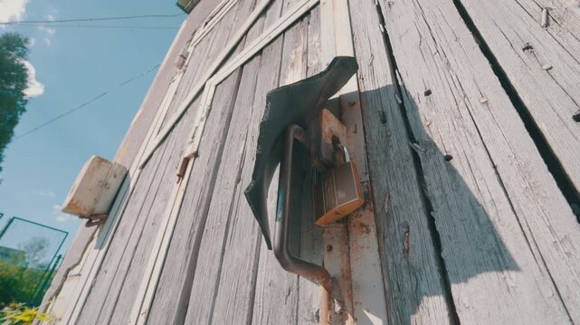 Old Wooden Shed Door with Padlock Covered by Rubber Strip | Bottom-Up Wide-Angle View of Weathered Locked Gate | Rustic Abandoned Rural Building