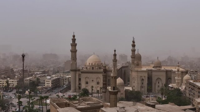 Two grand Cairo mosques with multiple minarets and imposing domes rise above the sprawling hazy cityscape of Egypt's capital, a symbol of Islamic heritage and history.