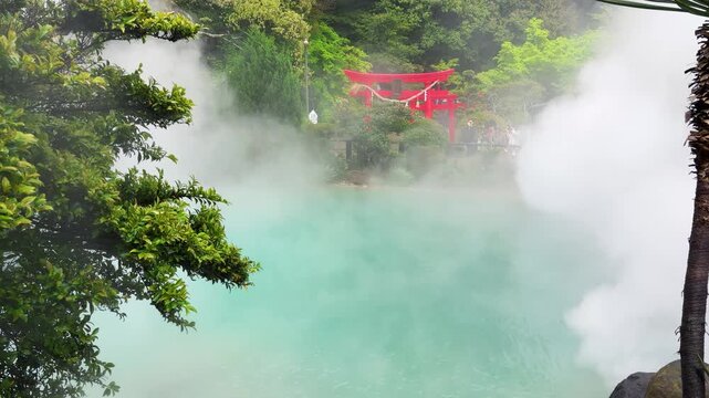 Steaming turquoise thermal hot spring Umi Jigoku in Beppu Japan surrounded by lush green trees. Red shinto torii gate stands on the edge of the steaming volcanic pond. 