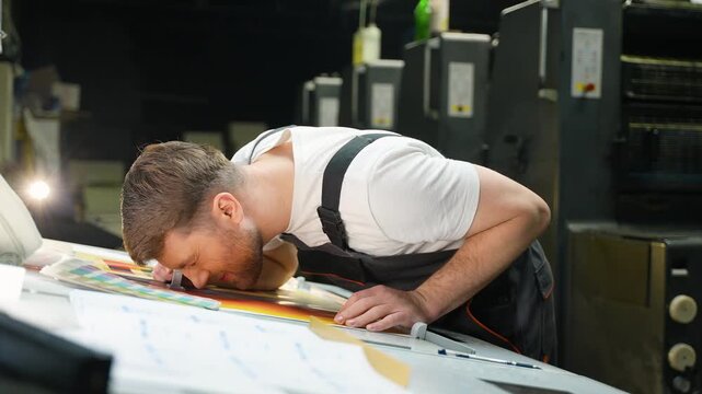 Male printer inspecting color quality print with magnifying glass