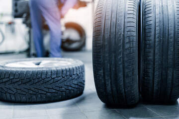 Stack of car tires next to mechanic in workshop. Service replacing wheel pads in garage. © Parilov