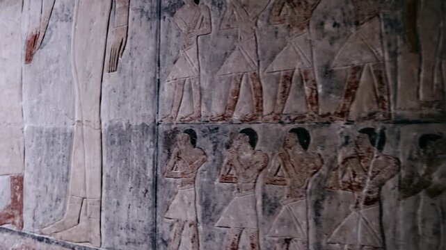 Corridor of Mereruka mastaba tomb at Saqqara, Egypt, with large painted red relief figure of tomb owner, smaller scene registers and dark doorway leading deeper inside.