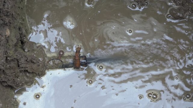 Underground pipe burst and water leaking into a dirty puddle. Close-up of a damaged plastic pipe underground, from which water is pouring under pressure. Emergency situation on utility networks, flood