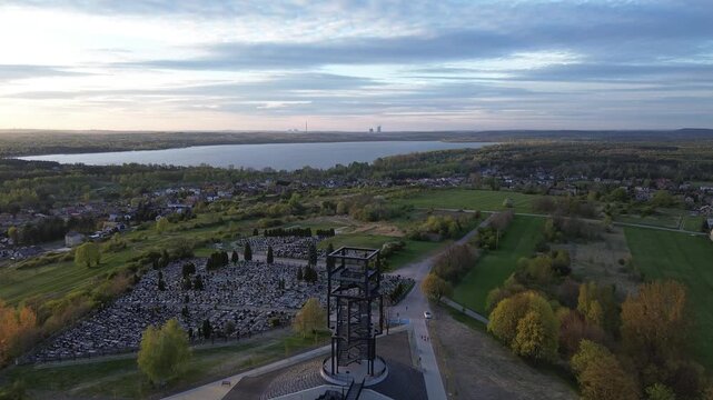 Aerial drone forward flight over observation tower and cemetery toward lake and industrial plant.
